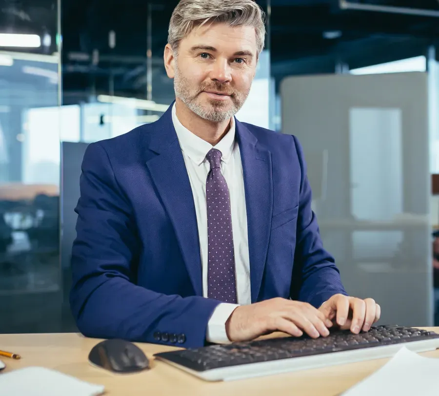 Executivo de terno azul sentado ao teclado em um escritório envidraçado